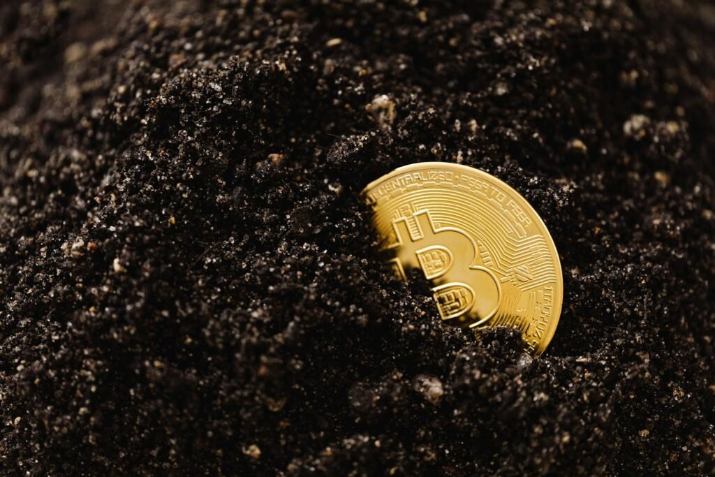 Golden Bitcoin partially buried in dark soil, symbolizing digital currency growth.
