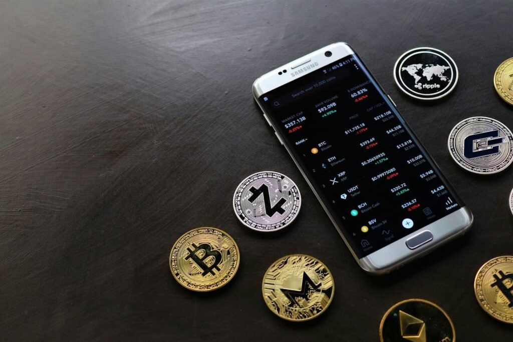 A collection of cryptocurrency coins and a smartphone displaying a digital trading platform.