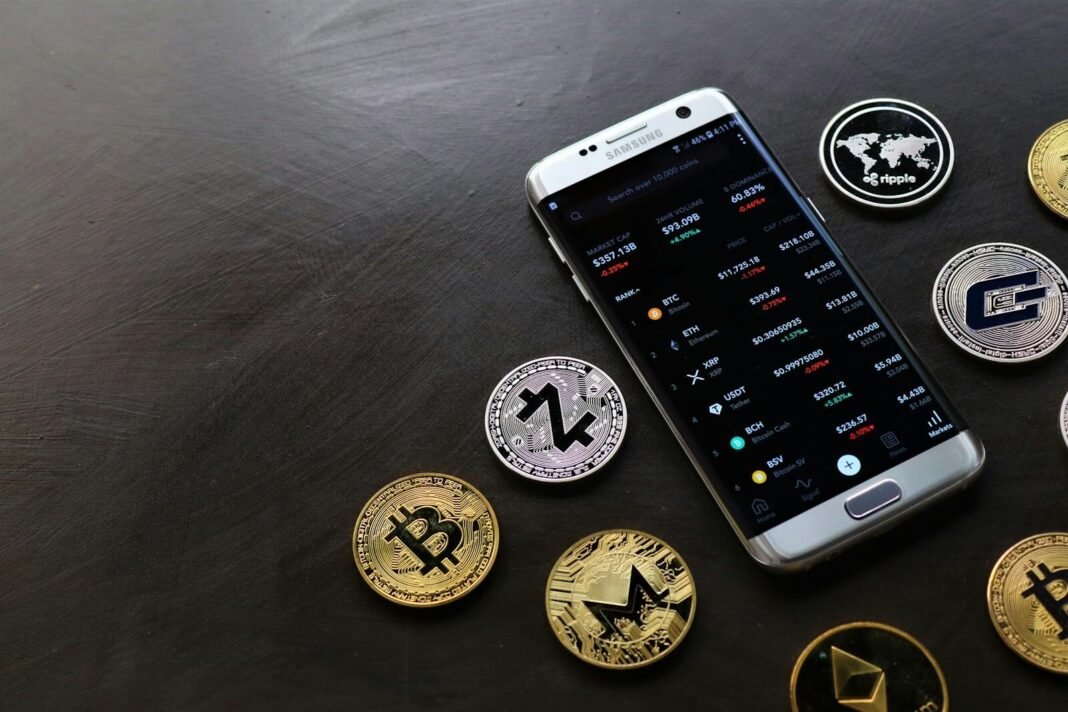 A collection of cryptocurrency coins and a smartphone displaying a digital trading platform.