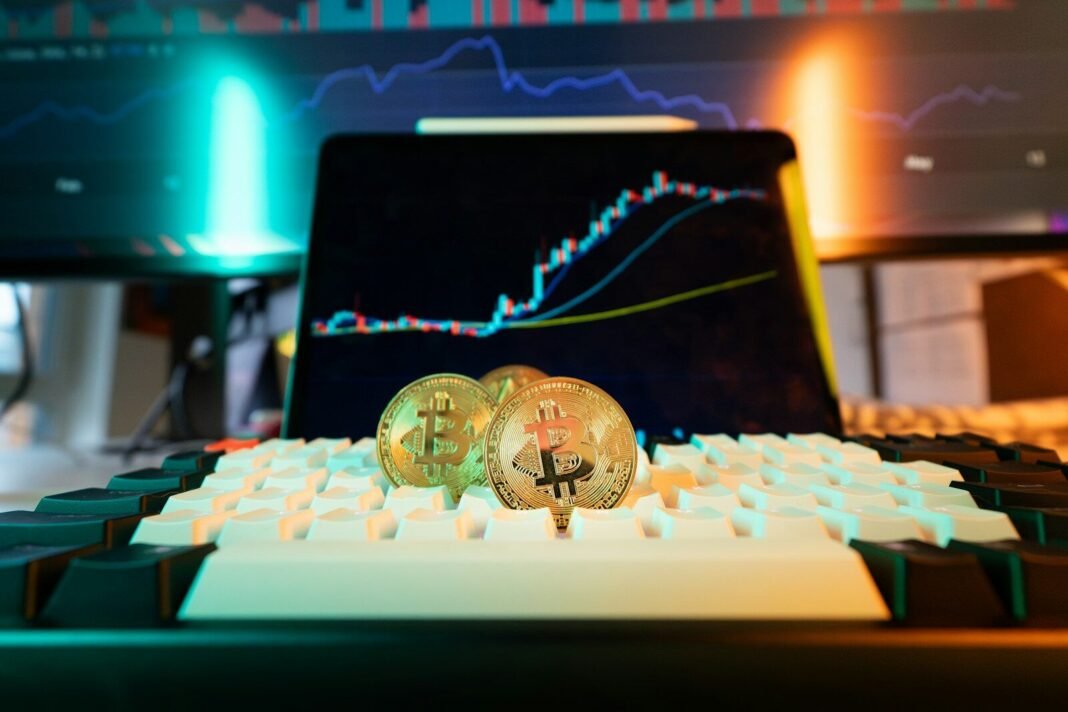 Bitcoin coins rest on a keyboard with stock charts.